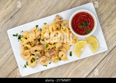 Frittierte Baby-Tintenfisch-Calamari-Ringe serviert als und Apertizer mit einer roten Sauce zum Dippen. Stockfoto