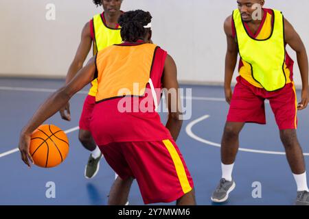 Drei afroamerikanische Männer in Sportuniformen, die Basketball spielen, üben auf dem Hallenplatz Stockfoto