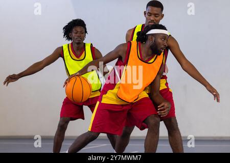Drei afroamerikanische Männer in Sportrikots, die auf dem Platz dribbeln und sich verteidigen Stockfoto