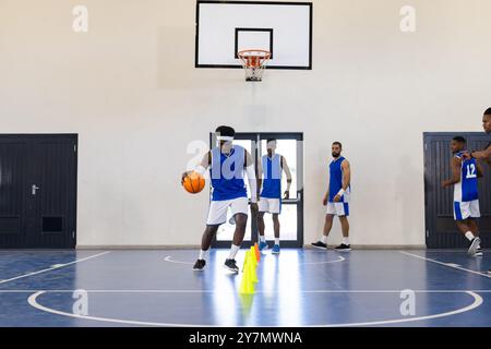 Dribbelt Basketball um Kegel, Spieler üben ihre Fähigkeiten auf dem Hallenplatz Stockfoto