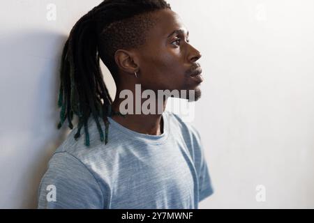 Profil eines Mannes mit Dreadlocks, der nachdenklich aussieht und ein lässiges blaues Hemd trägt Stockfoto