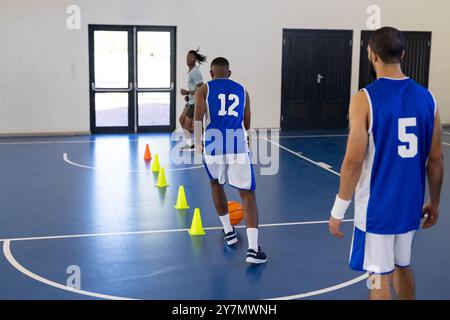 Dribbeln von Basketball um Kegel, Spieler üben ihre Fähigkeiten auf dem Hallenplatz, Kopierraum Stockfoto