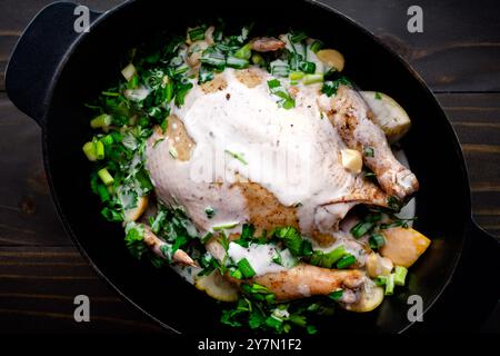 Ungekochtes Huhn in einem niederländischen Ofen mit Kräutern und Kokosmilch: Rohe Huhn in einem gusseisernen Topf mit Kokosmilch, Koriander, Zwiebeln und Zitronenscheiben Stockfoto