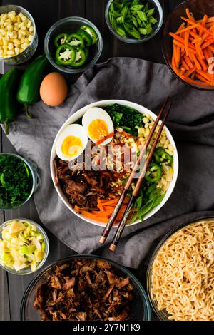 Schweineramen mit Gemüse und einem hart gekochten Ei: Ramen-Nudeln mit Karotten, Zwiebeln, Paprika und mehr in einer Schüssel mit Stäbchen serviert Stockfoto