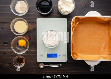 Wiegen von Mehl auf einer digitalen Waage, umgeben von Zutaten: Kaffee, Eigelb, Kondensmilch, Frischkäse und anderen Zutaten für den Kaffeewirbel Stockfoto