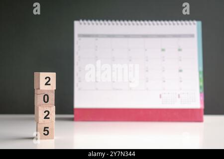 2025 auf Holzwürfeln mit Kalender im Hintergrund. Kopierbereich. Neues Jahr, Neubeginn. Stockfoto