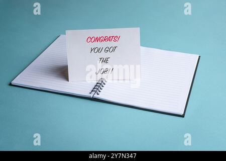 Herzlichen Glückwunsch, dass Sie den Job bekommen haben, eine Nachricht auf einer weißen Karte auf einem Notizblock. Neues Beschäftigungs- oder Beschäftigungskonzept. Stockfoto