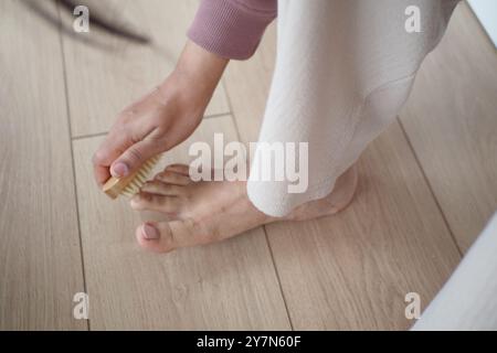 Mit einer Bürste bürstet die Person sanft ihren Fuß auf den Hartholzboden Stockfoto