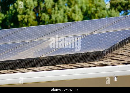 Nahaufnahme von Solarpaneelen auf einem Dach mit braunen Schindeln. Eine Solarstromanlage, die auf einem schrägen Dach installiert ist, ist von Netzen umgeben, die Schutz bieten Stockfoto