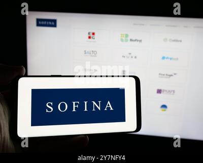 Person mit Smartphone und Logo der belgischen Holdinggesellschaft Sofina SA auf dem Bildschirm vor der Website. Schwerpunkt auf dem Display des Telefons. Stockfoto