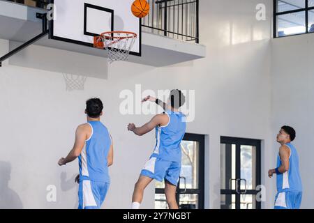 Basketball spielen, drei junge Männer in blauen Uniformen schießen drinnen Basketball Stockfoto