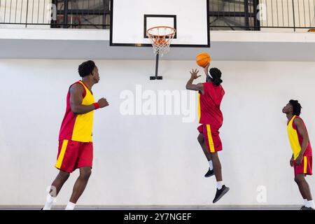 Drei Spieler in roten und gelben Uniformen spielen Basketball und zielen auf den Korb Stockfoto