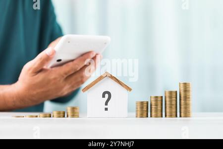 Der Mensch verwendet einen Taschenrechner, um häusliche Zahlen wie Steuern und Hypothekenzinsen zu berechnen, mit einem Stapel Münzen und einem Hausmodell neben ihm. Das ima Stockfoto