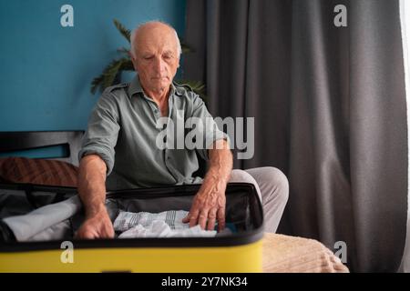 Ein Mann, der sein Gepäck in einem Reisesaal packt. Seniorenreisender freut sich, im Urlaub zu sein Stockfoto