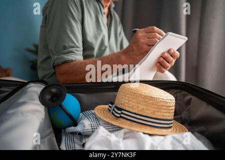 Urlaubs-, Urlaubs- und Reisekonzept. Reisender Senior man hält eine Checkliste und bereitet Sachen im Gepäck für die Reise zu Hause vor Stockfoto