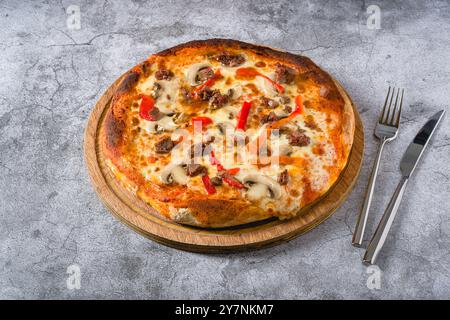 Pizza mit Paprika und Roastbeef auf dem Schneidebrett auf einem Steintisch Stockfoto