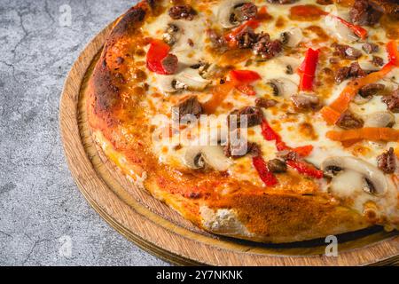 Pizza mit Paprika und Roastbeef auf dem Schneidebrett auf einem Steintisch Stockfoto