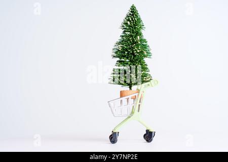 Der farbenfrohe grüne Einkaufswagen enthält einen kleinen Weihnachtsbaum, der das Weihnachtsgeschäft symbolisiert. Perfekt für Designs und Werbung im Urlaubsstil. Stockfoto