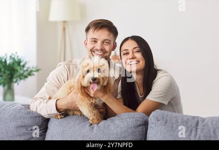 Porträt eines glücklichen lachenden jungen Paares nahe der Couch mit süßem kleinen Hund, Mann und Frau Stockfoto