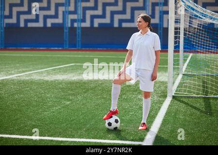 Mädchen-Fußballspielerin in weißen Shorts und roten Stiefeln, die mit Fußball auf einem grünen Kunstrasenfeld stehen. Frauenfußball-Konzept Stockfoto