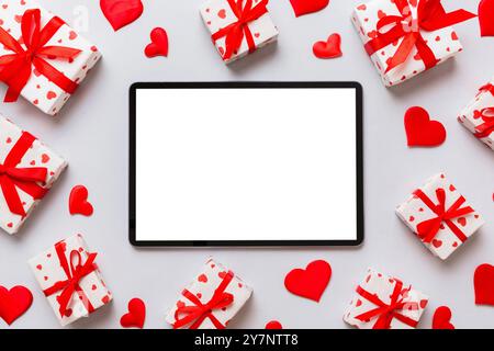 Draufsicht des digitalen Tablets mit Geschenkboxen und Herzen auf farbenfrohem Hintergrund. Tablet mit schwarzem Bildschirm mit Weihnachtsdekoration Geschenkbox, Draufsicht. Stockfoto
