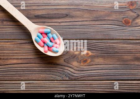 Vitaminkapseln in einem Löffel auf farbigem Hintergrund. Pillen als gesunde Mahlzeit serviert. Rote weiche Gel Vitamin-Supplement-Kapseln auf Löffel. Stockfoto