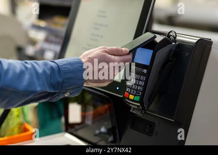 Die Person bezahlt kontaktlos per Smartphone an der Kasse des Stores. Technologie ermöglicht bequeme und sichere Transaktionen im Einzelhandel. Konzentrieren Sie sich darauf, das Telefon über das Zahlungsterminal zu halten. Stockfoto