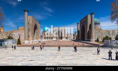 Samarkand, Usbekistan - 25. März 2024: Touristen spazieren an einem sonnigen Tag auf dem Registan-Platz. Drei Madrasas von links nach rechts: Ulugh Beg Madrasah Stockfoto