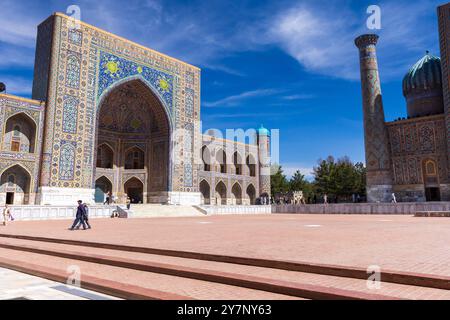 Samarkand, Usbekistan - 25. März 2024: Touristen spazieren an einem sonnigen Tag auf dem Registan-Platz. Tilya-Kori Madrasah befindet sich auf der linken Seite Stockfoto