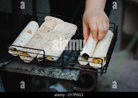 Kochen unter freiem Himmel. Eine Frau kocht Pita Tortillas auf einem Grillfeuer im Freien. Vegetarische Grillgerichte. Handgerollte Gemüsepackungen. Stockfoto