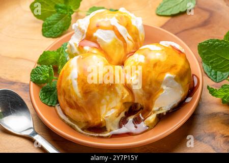 Drei Kugeln Vanilleeis mit Karamell-Belag und frischen grünen Minzblättern auf einem Holztisch. Stockfoto