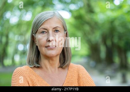 Reife Frau mit grauem Haar, die selbstbewusst im Freien steht. Ruhe und Weisheit zum Ausdruck bringen. Sonniger Tag sorgt für Wärme. Perfekte Darstellung von Selbstvertrauen und Gelassenheit in der Natur. Stockfoto