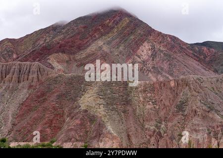 Niedrige Wolken über den gestreiften Gesteinsschichten eines Berges auf der anderen Seite des Flusses von Purmamarca, Argentinien. Stockfoto