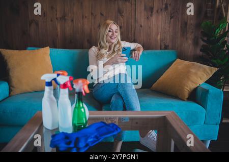 Foto von hübsch fröhlich Dame tragen lässiges Hemd tun Frühling aufräumen SMS modernes Gerät drinnen Raum Haus Stockfoto