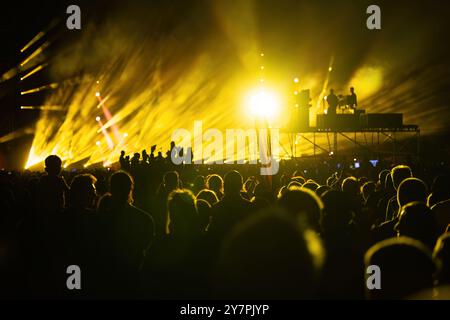 Bühnenlichter defokussieren Bokeh-Hintergrund bei einem Musikkonzert und Silhouetten, in denen Menschen in der Menge gefeiert werden Stockfoto