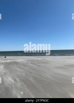 Eine ruhige Strandszene mit glattem Sand und einem klaren blauen Himmel, mit einem ruhigen Ozean im Hintergrund. Stockfoto
