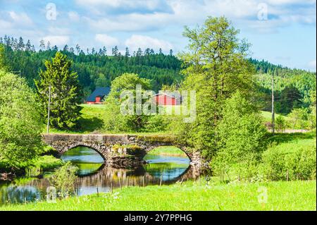 Eine malerische Aussicht auf eine historische Steinbrücke, die einen ruhigen Fluss überquert. Grüne Bäume umgeben die Gegend, während traditionelle rote Gebäude Charme und Charme verleihen Stockfoto