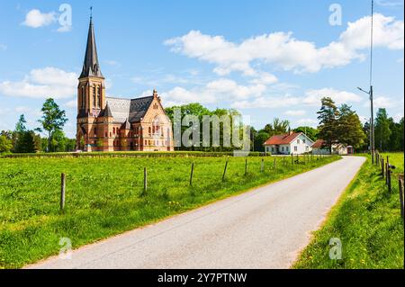 Eine friedliche Straße schlängelt sich durch die schwedische Landschaft, die zu einer wunderschön gestalteten Kirche führt, eingebettet zwischen üppigem Grün und malerischen Häusern, al Stockfoto