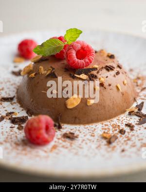 Dunkle Schokoladenflan mit Mandeln. Dekoriert mit Kakaopulver und Himbeeren. Stockfoto