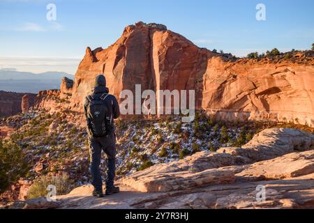 Ein männlicher Wanderer steht am Rande einer Klippe im Canyonlands National Park von Utah und bewundert die atemberaubende Aussicht auf die schneebedeckte Landschaft. Stockfoto