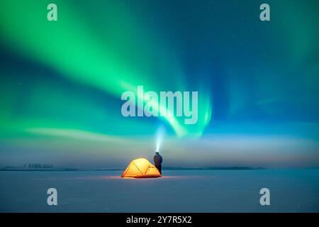 Tourist mit Taschenlampe in der Nähe des gelben Zelt vor dem Hintergrund des unglaublichen Sternenhimmels mit Aurora Borealis. Wunderschöne Nachtlandschaft mit Polarlichtern. Nordlichter im Winterfeld Stockfoto