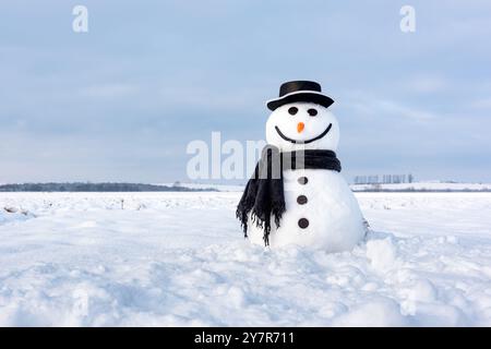 Lustiger Schneemann in stylischem schwarzen Hut und schwarzem Schal auf verschneiten Feldern. Frohe Weihnachten und frohes neues Jahr Stockfoto