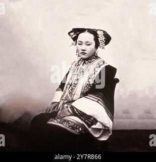 Vintage-Foto von Mandschu-Dame. Nord-Zhili (Provinz Pei-chih-li oder Peking). 1869 (von John Thomson, 1837–1921) Eine Frau mit einem raffinierten Haarschnitt, die eine bestickte Jacke mit langen, breiten Ärmeln trägt. Sie sitzt, posiert nach links, blickt nach vorne, vor einem hellen Hintergrund Stockfoto