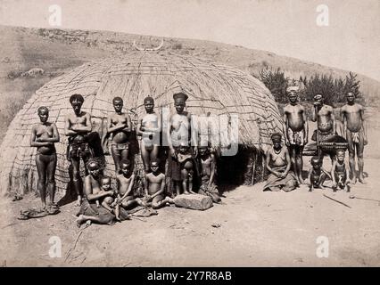 Vintage-Foto von Einheimischen und Kraal. Afrikaner vor einer traditionellen Kraal-Hütte. Südafrika, zwischen 1800 und 1899. Kraal (auch Kraal oder Kraul) ist ein Afrikaans- und niederländisches Wort, das auch im Südafrikanischen Englisch verwendet wird, für ein Gehege für Rinder oder anderes Vieh, das sich innerhalb einer Siedlung oder eines Dorfes im südlichen Afrika befindet, umgeben von einem Zaun aus Dornbuszweigen, einer Palisade, einer Schlammmauer oder anderen Umzäunungen, die in etwa kreisförmiger Form sind. Sie ähnelt einem Boma in Ost- oder Zentralafrika. Stockfoto