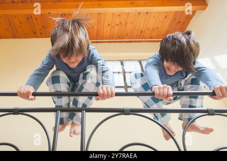 Zwei kleine Kinder haben Spaß am Geländer eines Bettes. Sie tragen einen blauen und weißen Pyjama. Beide halten sich an der Schiene fest und springen Stockfoto