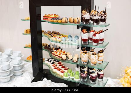 Ein Tisch voller Desserts mit einer Vielzahl von Aromen und Farben. Die Desserts werden in kleinen Plastikbechern serviert. Der Tisch ist für eine Party eingerichtet. Stockfoto