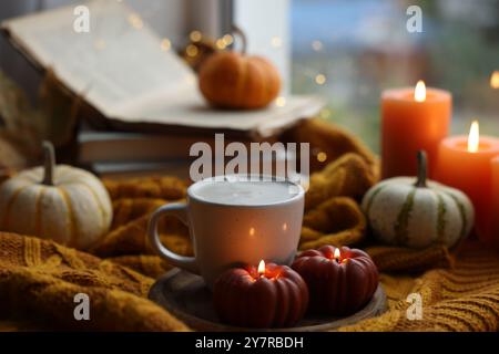 Tasse Kaffee und brennende Kerzen in Kürbisform auf weichem Pullover. Herbstatmosphäre Stockfoto