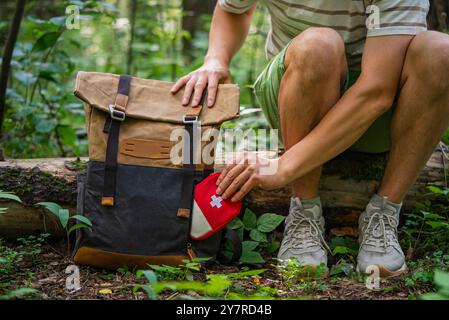 Ein Mann, der ein erste-Hilfe-Set in seinen Wanderrucksack legt, während er sich im Wald ausruht und sich auf Outdoor-Abenteuer vorbereitet. Stockfoto