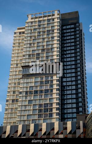 Blick aus der Nähe auf ein modernes Hochhaus mit reflektierenden Fenstern vor einem klaren, blauen Himmel. Die Architektur zeigt zeitgenössische urbane Elemente Stockfoto
