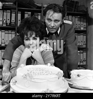 Ein Happy Birthday Lächeln von Schauspielerin ELIZABETH TAYLOR, während sie mit ihrem Mann und Schauspieler RICHARD BURTON vor einer Geburtstagskuche posiert, die von der Crew von Burtons neuem Film Where Eagles Dare bereitgestellt wird, der derzeit in den MGM British Studios in der Nähe von London gedreht wird. Viele der Crew hatten mit der Schauspielerin - heute 36 - an früheren Bildern gearbeitet. Die Burtons leben derzeit auf einer 200-Fuß-Luxusyacht, die in der Themse vertäut ist. Die Jacht ist einfach eine Hundehütte für ihre vier Hunde, die wegen Quarantänebestimmungen keine Pfoten an Land setzen können. 27. Februar 1968 Stockfoto